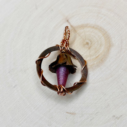Jewelry pendant with a purple flower on a textured wooden background
