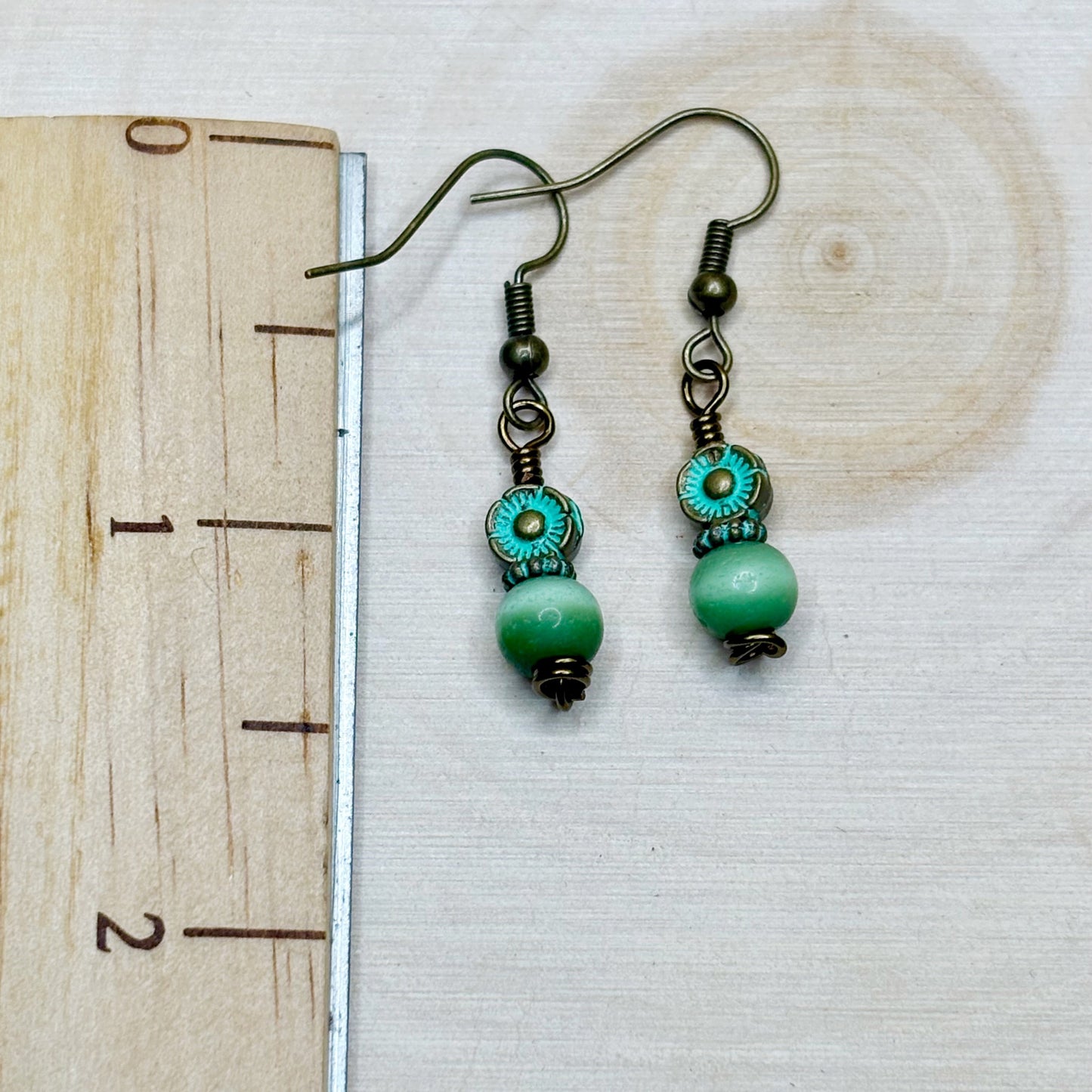 Green beaded earrings on a wooden surface with a ruler for scale.