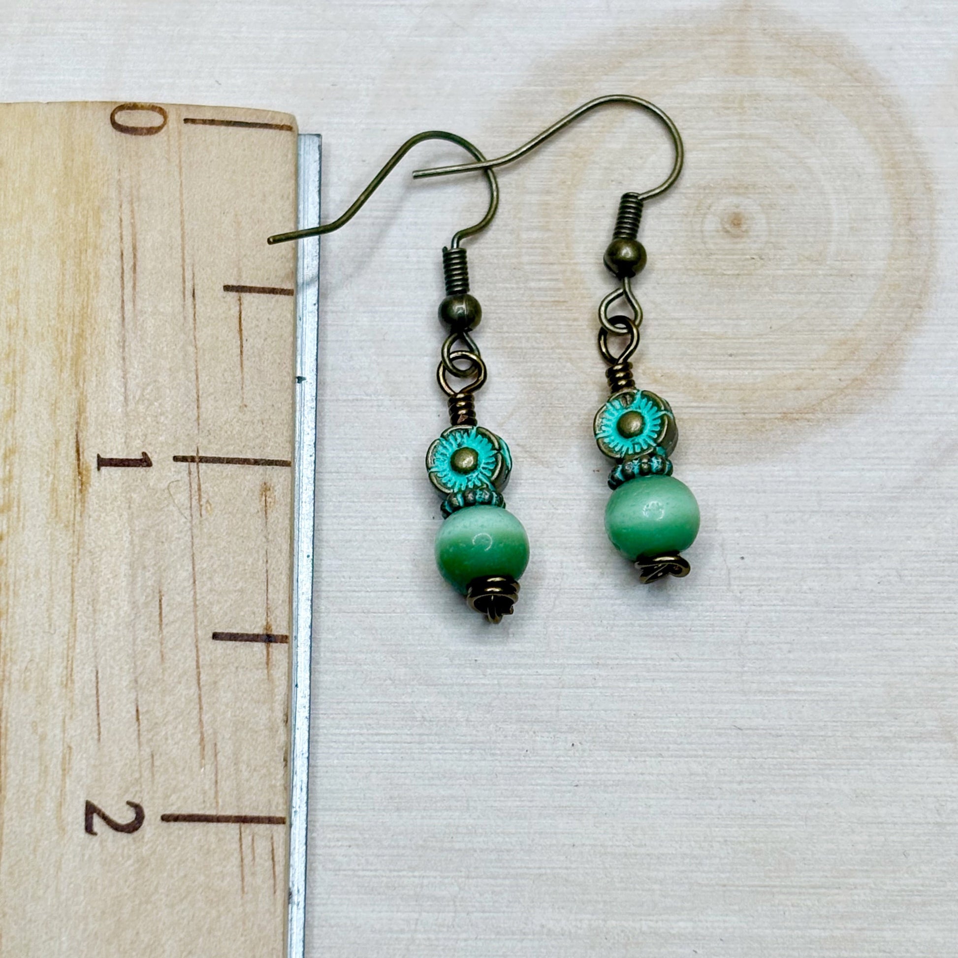 Green beaded earrings on a wooden surface with a ruler for scale.