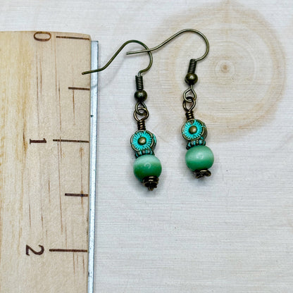 Green beaded earrings on a wooden surface with a ruler for scale.