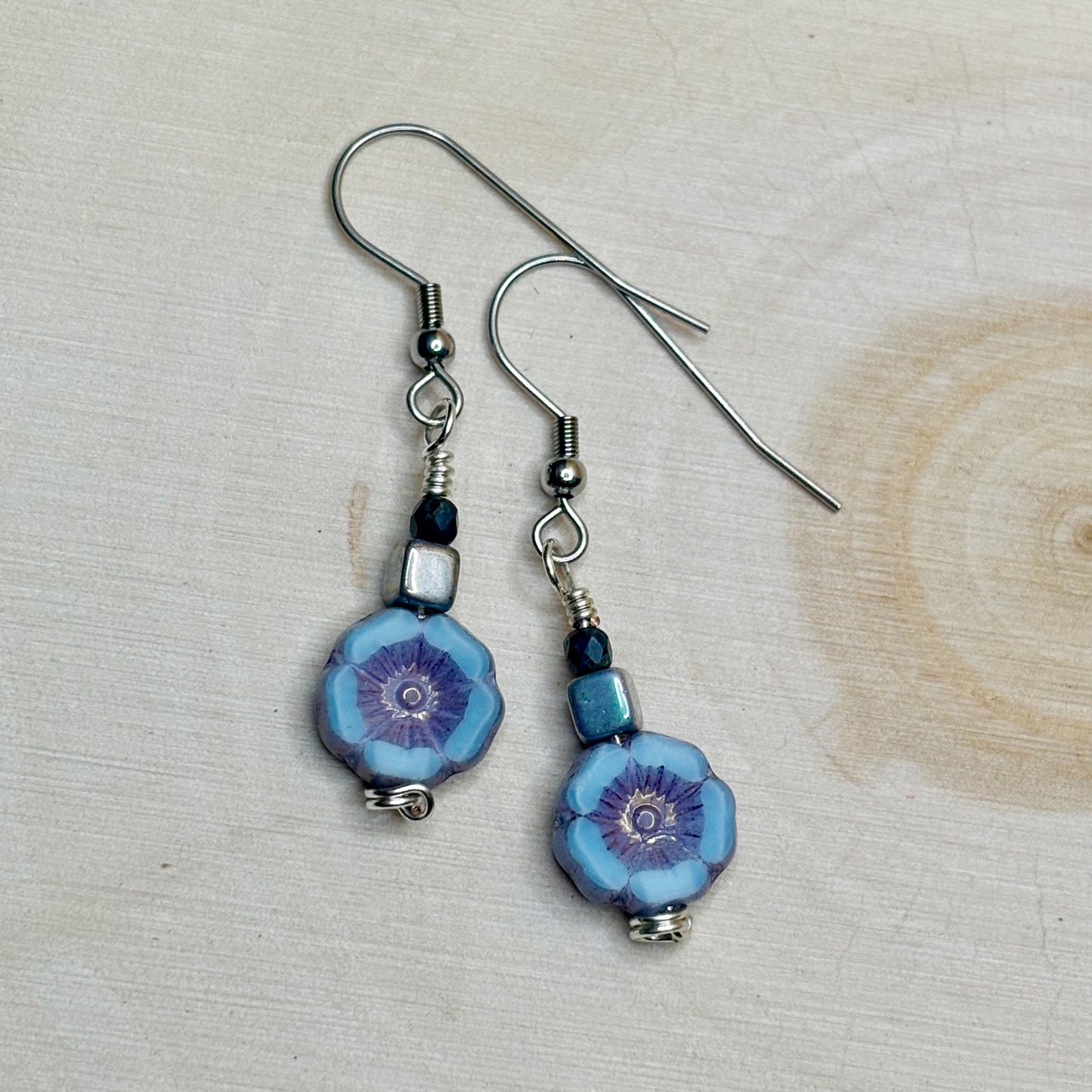 Pair of blue floral earrings with silver hooks on a light wooden surface