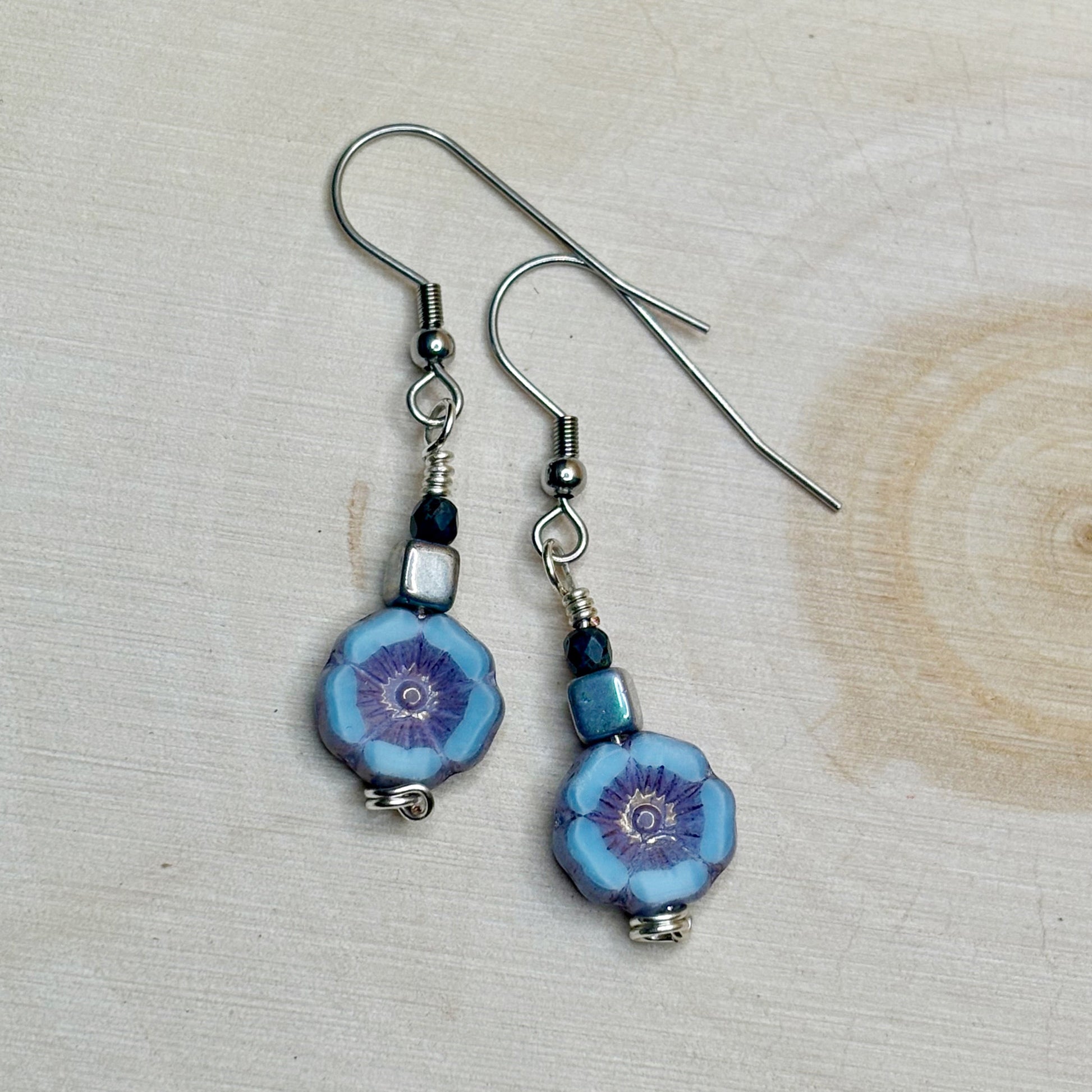 Pair of blue floral earrings with silver hooks on a light wooden surface