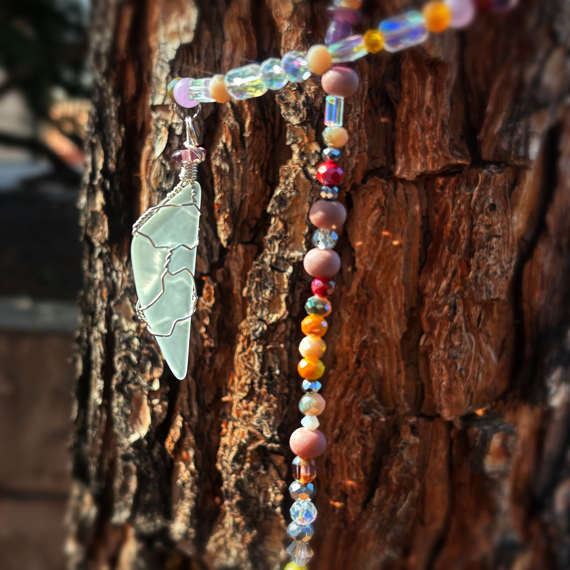 Colorful beaded sun catcher with a glass pendant on a tree trunk