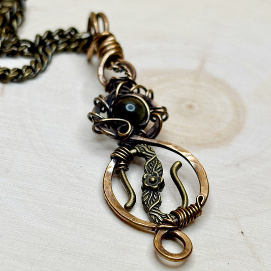 Bronze floral pendant on a chain against a light background