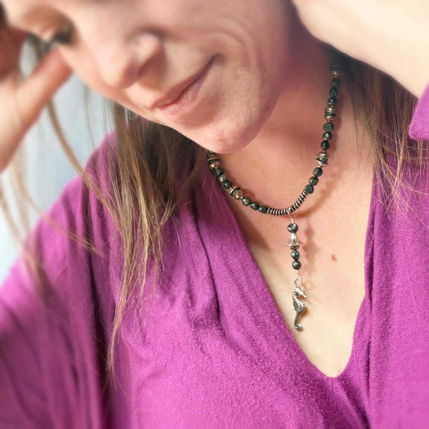 Woman wearing a purple shirt and a necklace with a green pendant.