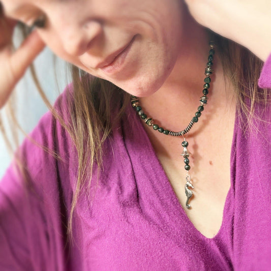 Woman wearing a purple shirt and a necklace with a green pendant.
