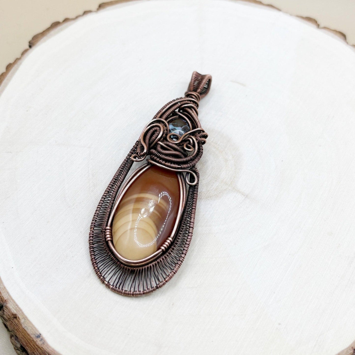 copper wire-wrapped pendant with a central stone on a white background