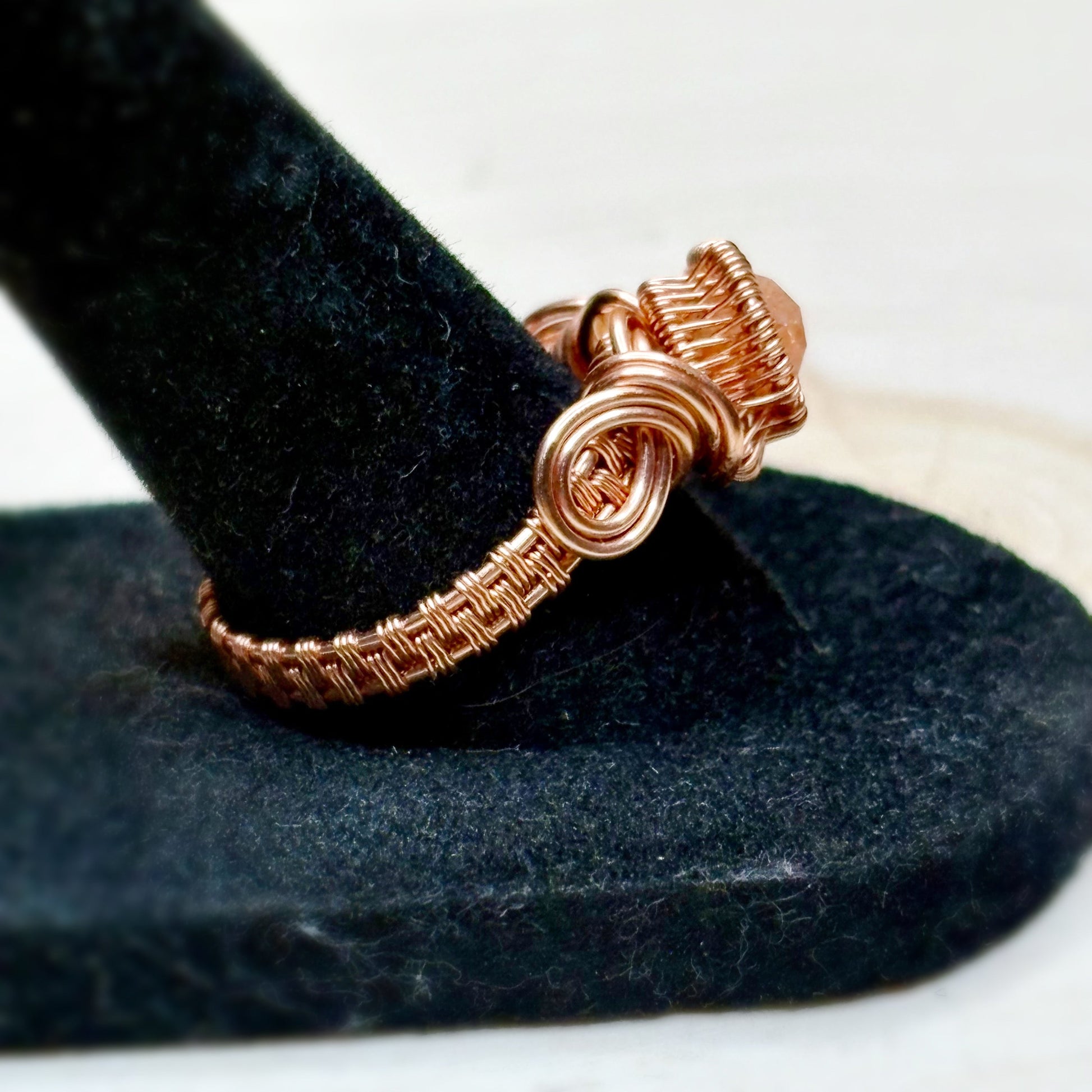 Copper wire-wrapped ring on a black stand with a white background