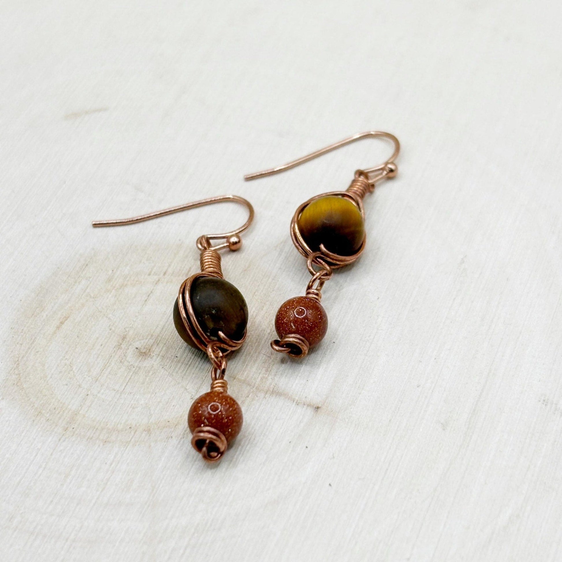 Pair of copper and brown bead earrings on a textured white wood surface