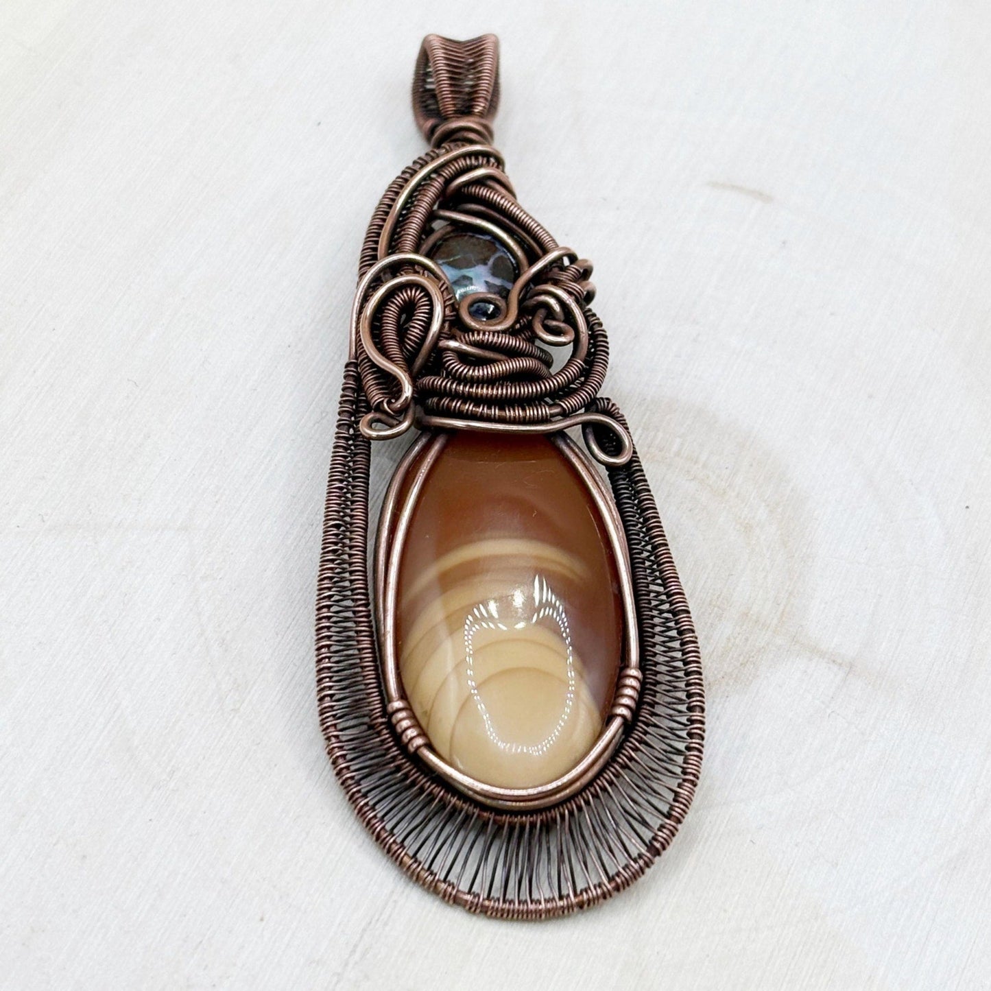 Decorative copper pendant with 2 stones opal and jasper in an antiqued copper frame sitting on a wooden background