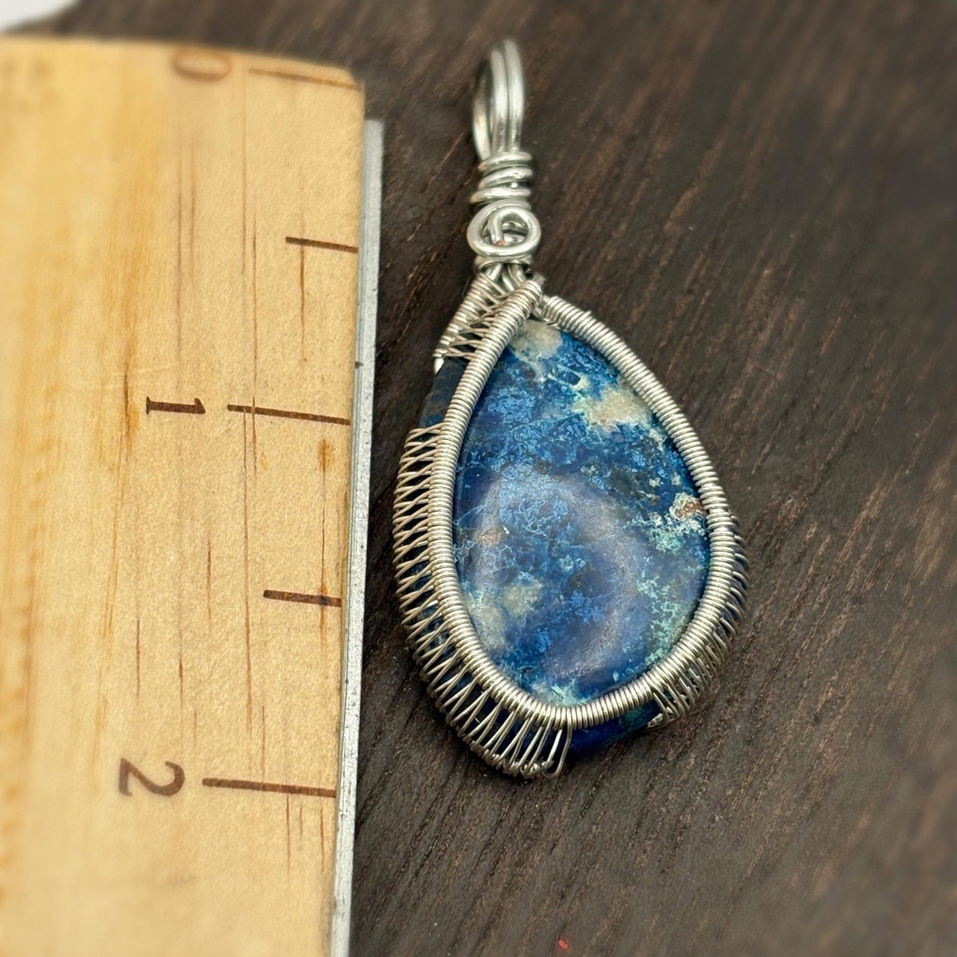 Blue stone pendant with silver wire wrapping on a wooden ruler