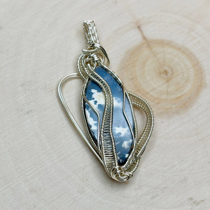 Silver wire-wrapped pendant with blue stone on a wooden surface