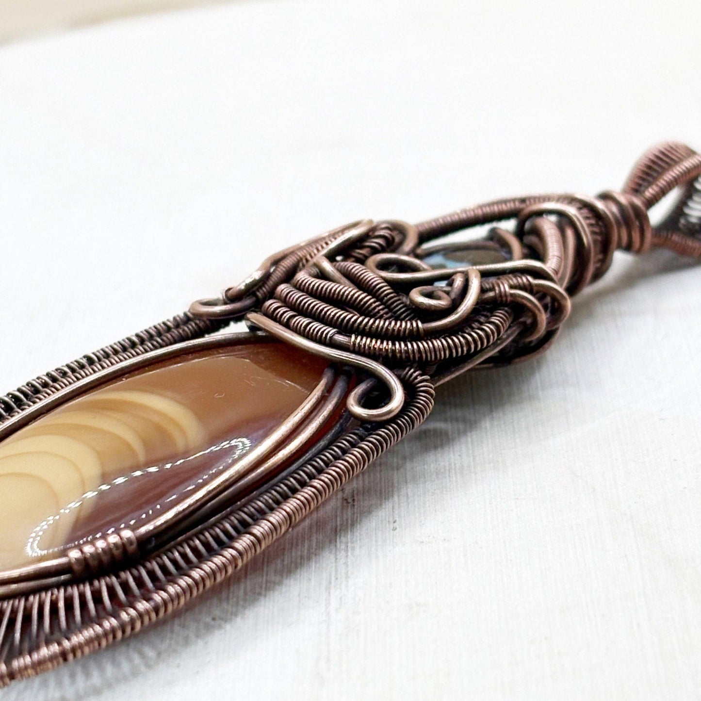 Copper-wrapped pendant with a central stone on a light background
