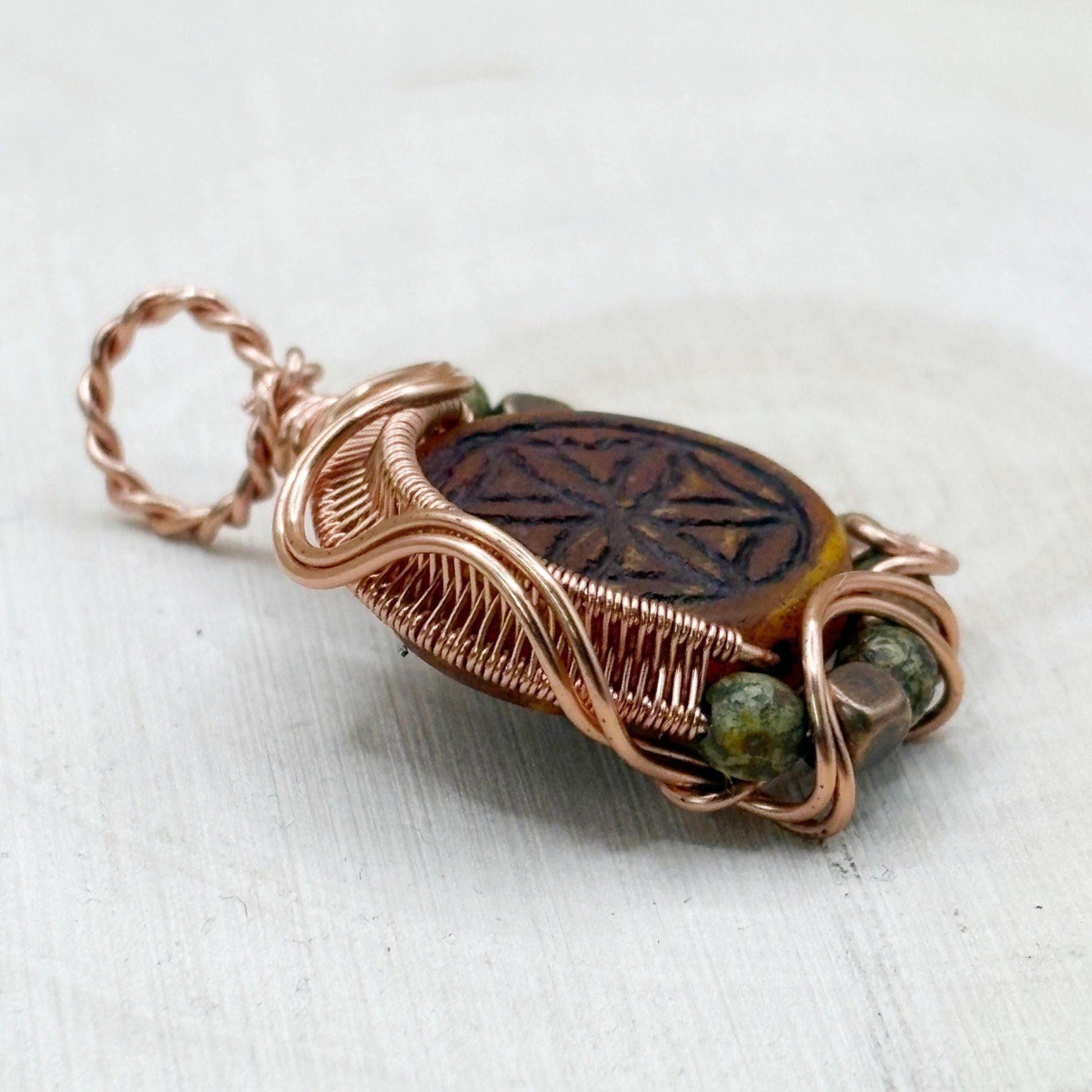 Copper-wrapped pendant with a central stone and green beads on a white background