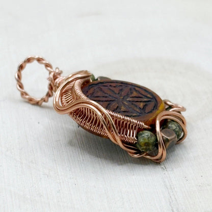 Copper-wrapped pendant with a central stone and green beads on a white background