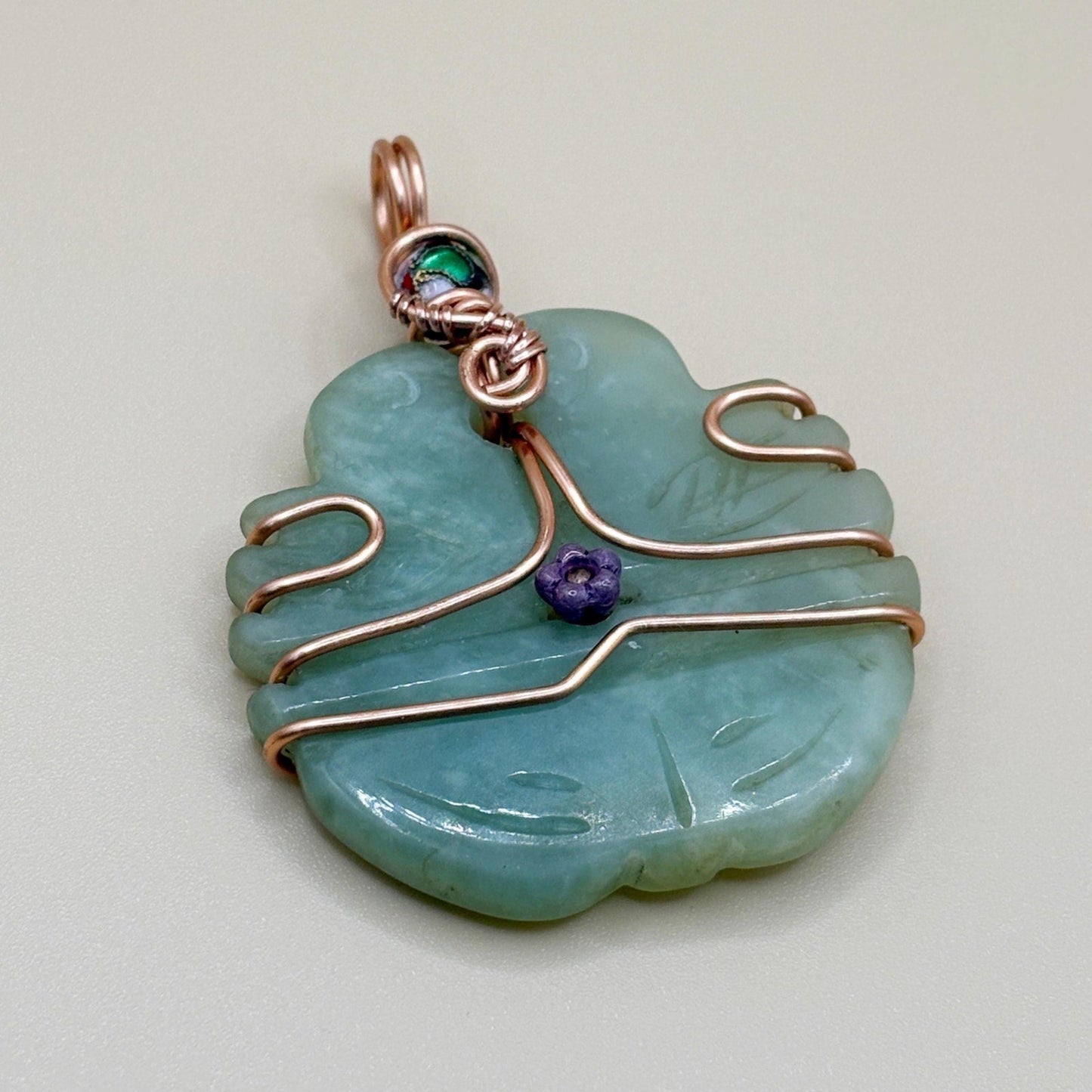 Jade stone pendant with copper wire wrapping on a light gray background