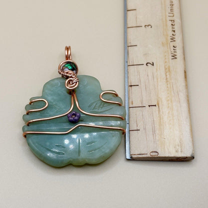 Green jade pendant with copper wire wrapping next to a wooden ruler for scale.