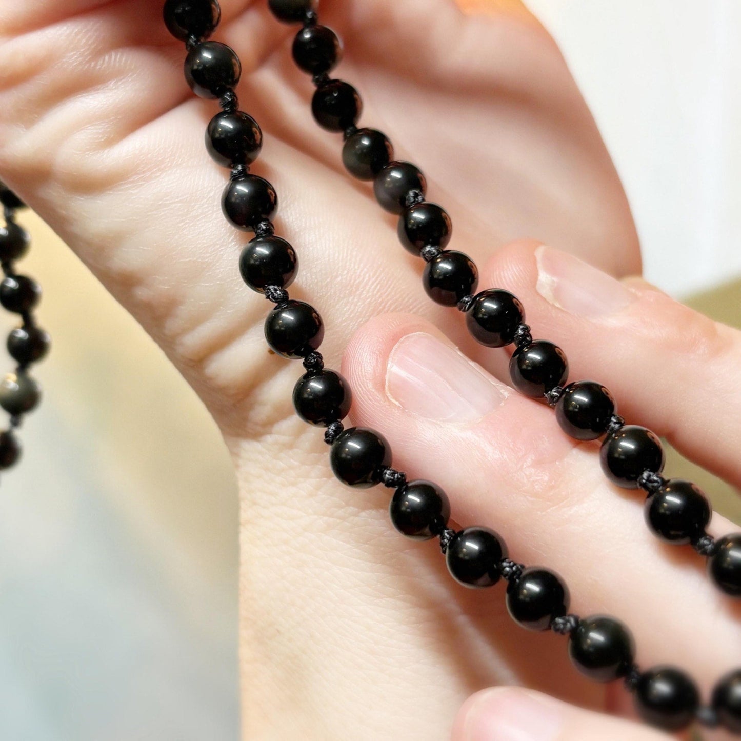Close-up of a hand holding a black beaded necklace.