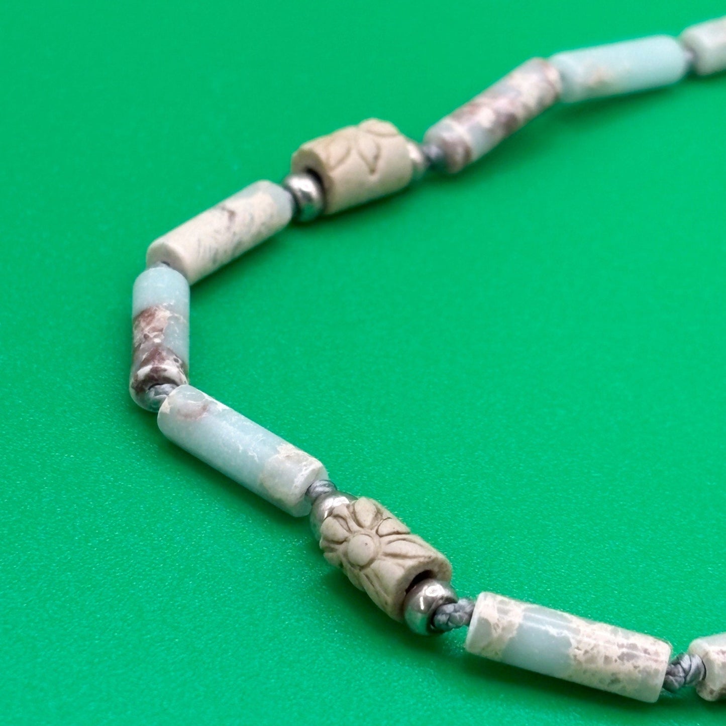Necklace with light blue and beige beads on a green background