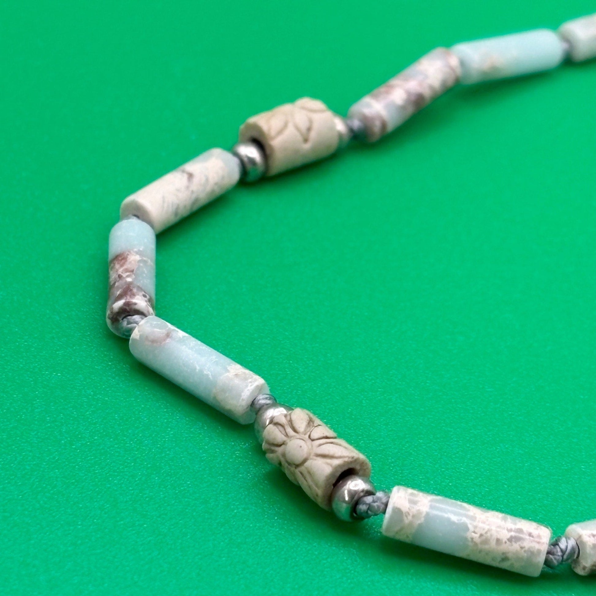 Necklace with light blue and beige beads on a green background