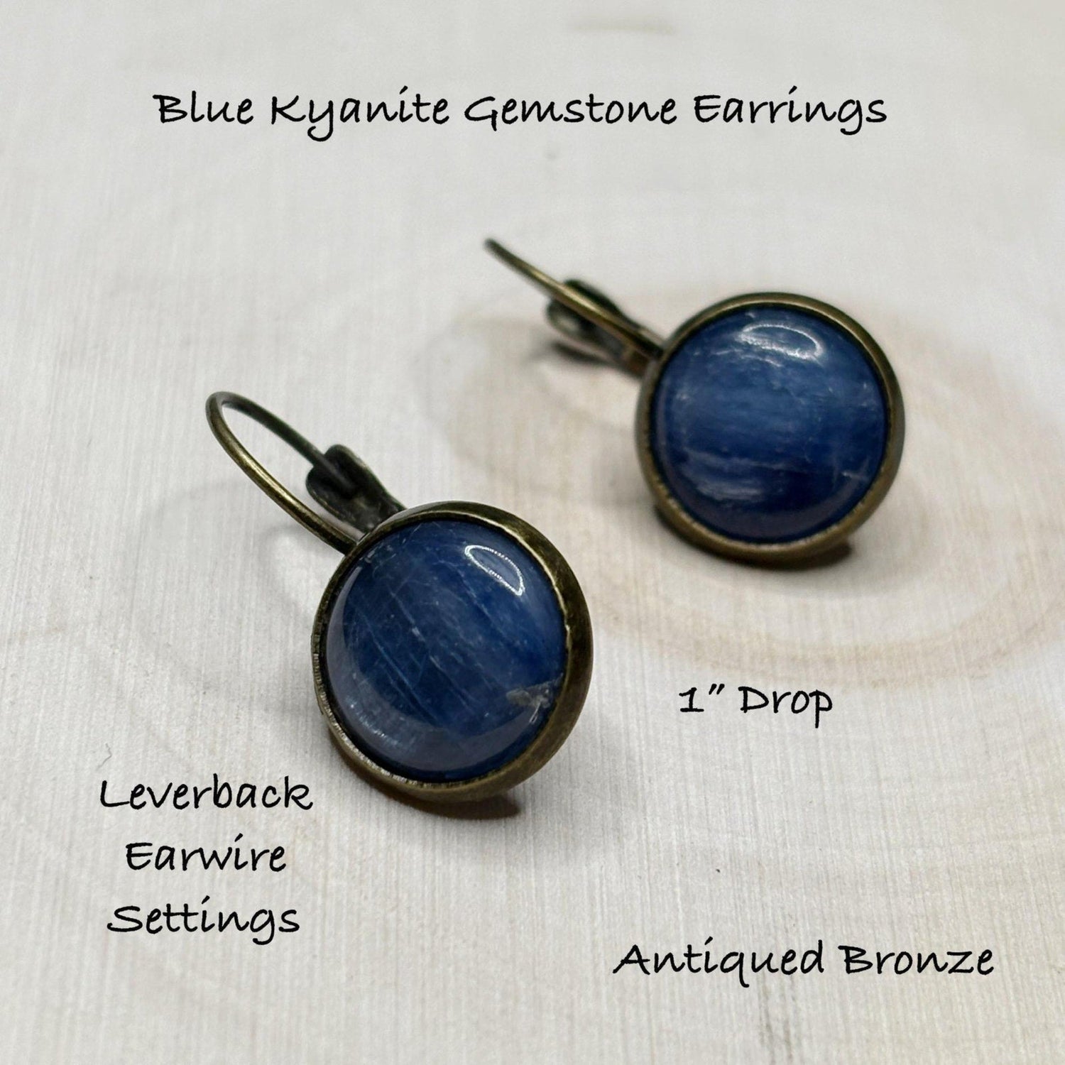 Blue kyanite gemstone earrings with antiqued bronze settings on a white wooden background.