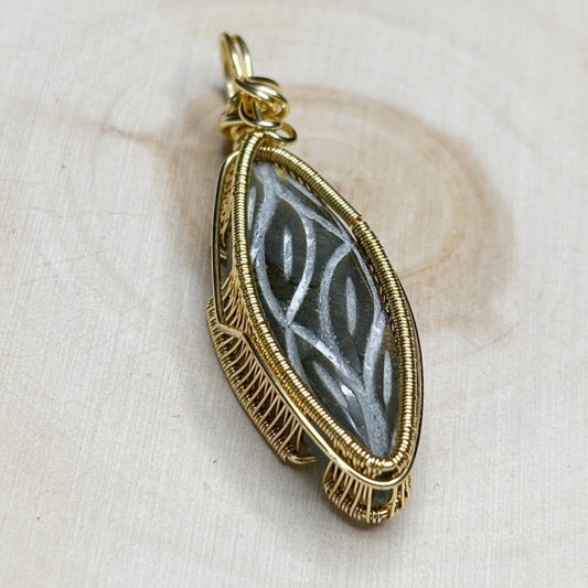 Gold-framed pendant with intricate design on a beige fabric background