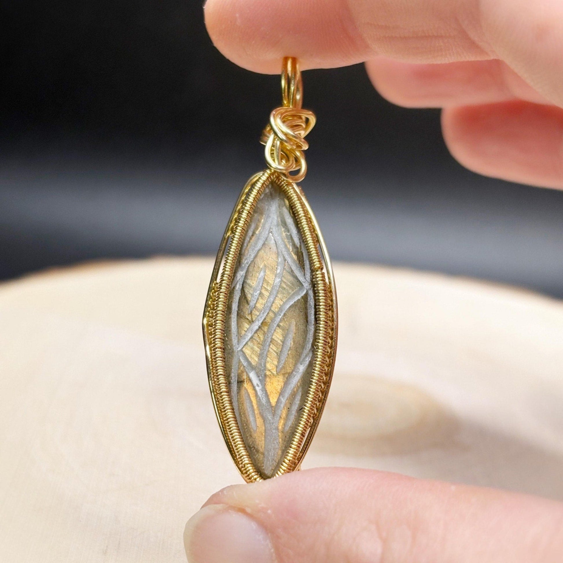 Gold pendant held between fingers against a neutral background