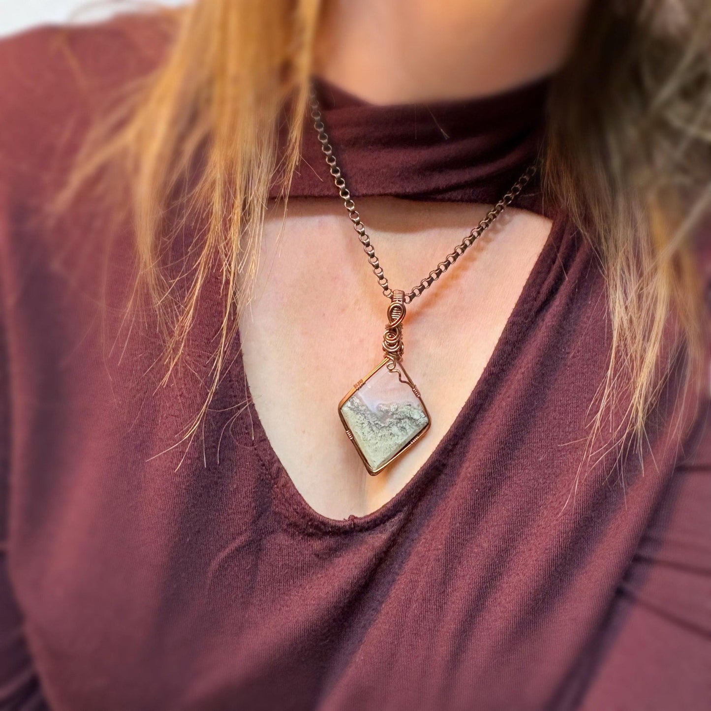 Necklace with a green pendant worn by a person in a maroon top.