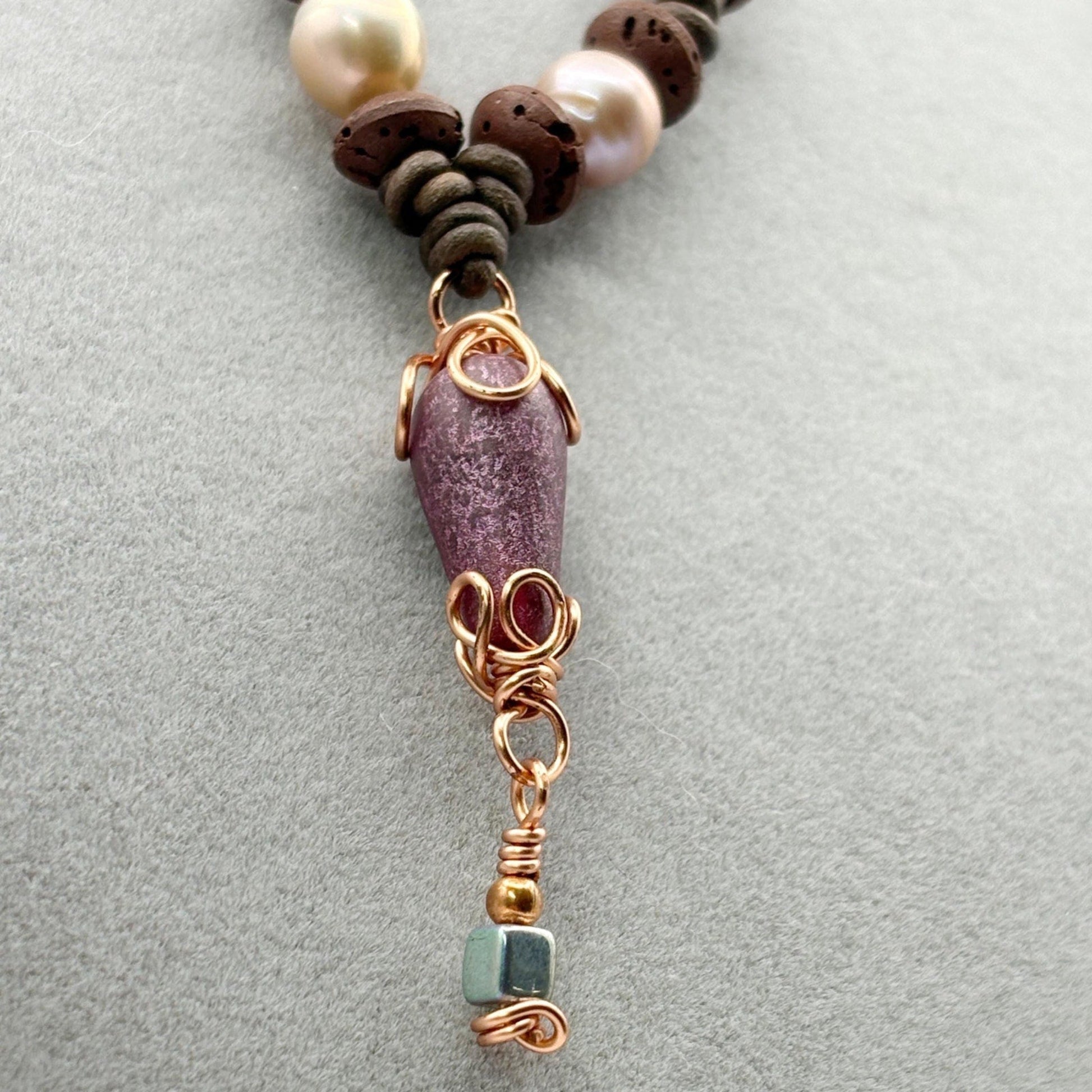 Necklace with brown beads, pink stone, and gold accents on a gray background