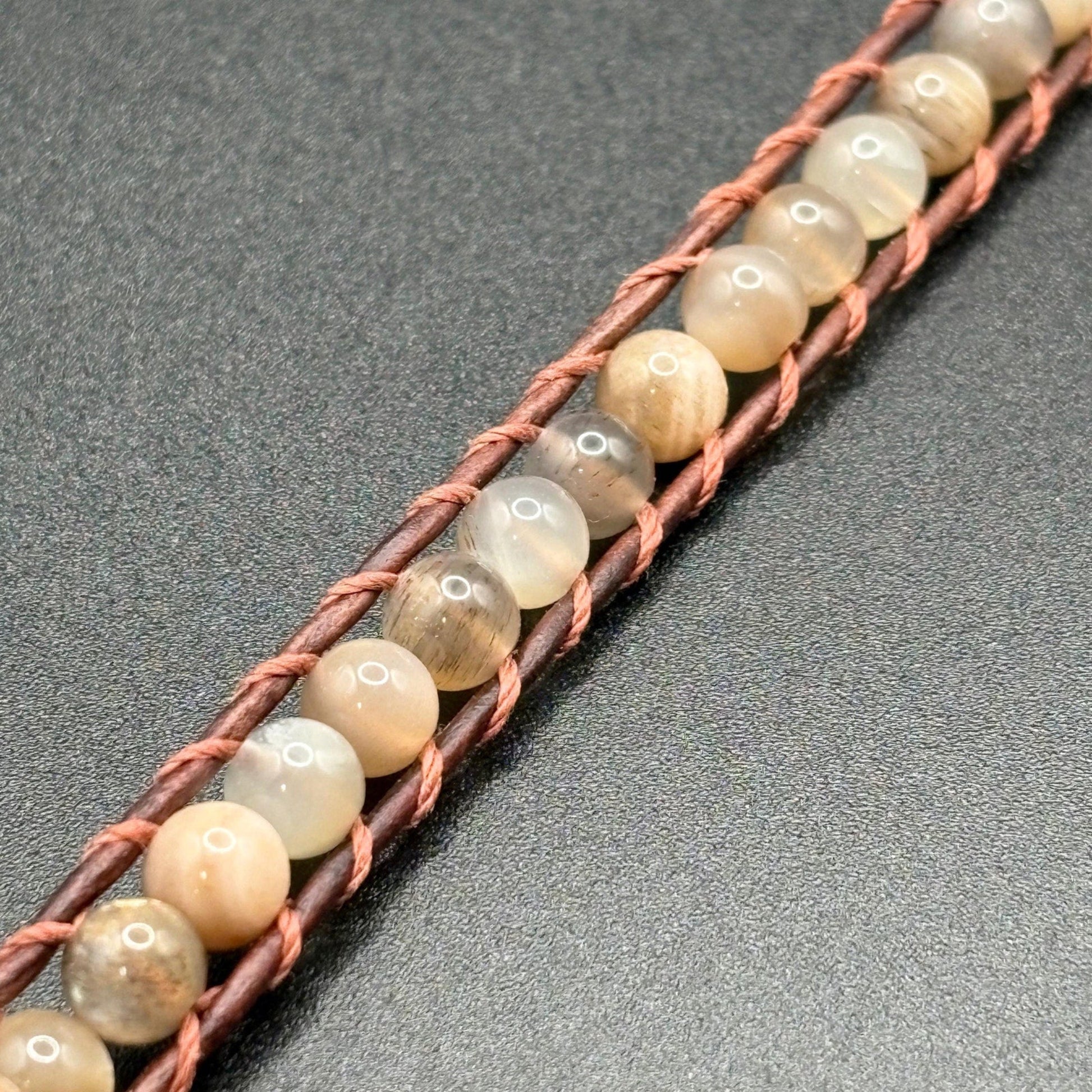 Beaded bracelet with brown cord on a gray background