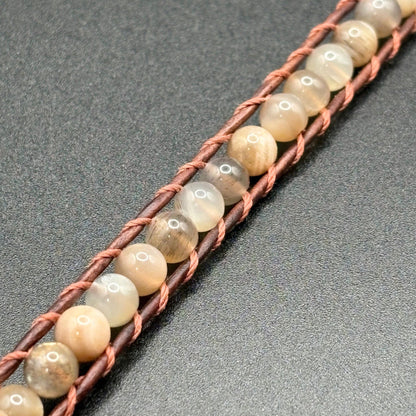 Beaded bracelet with brown cord on a gray background
