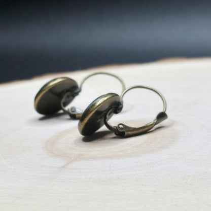 Pair of bronze-colored earrings on a wooden surface with a dark background