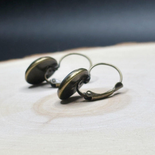 Pair of bronze-colored earrings on a wooden surface with a dark background