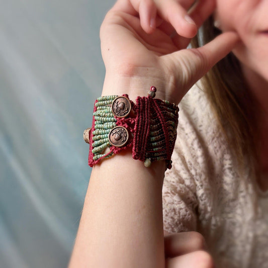 Close-up of a hand wearing a red and green macrame bracelet with buttons.