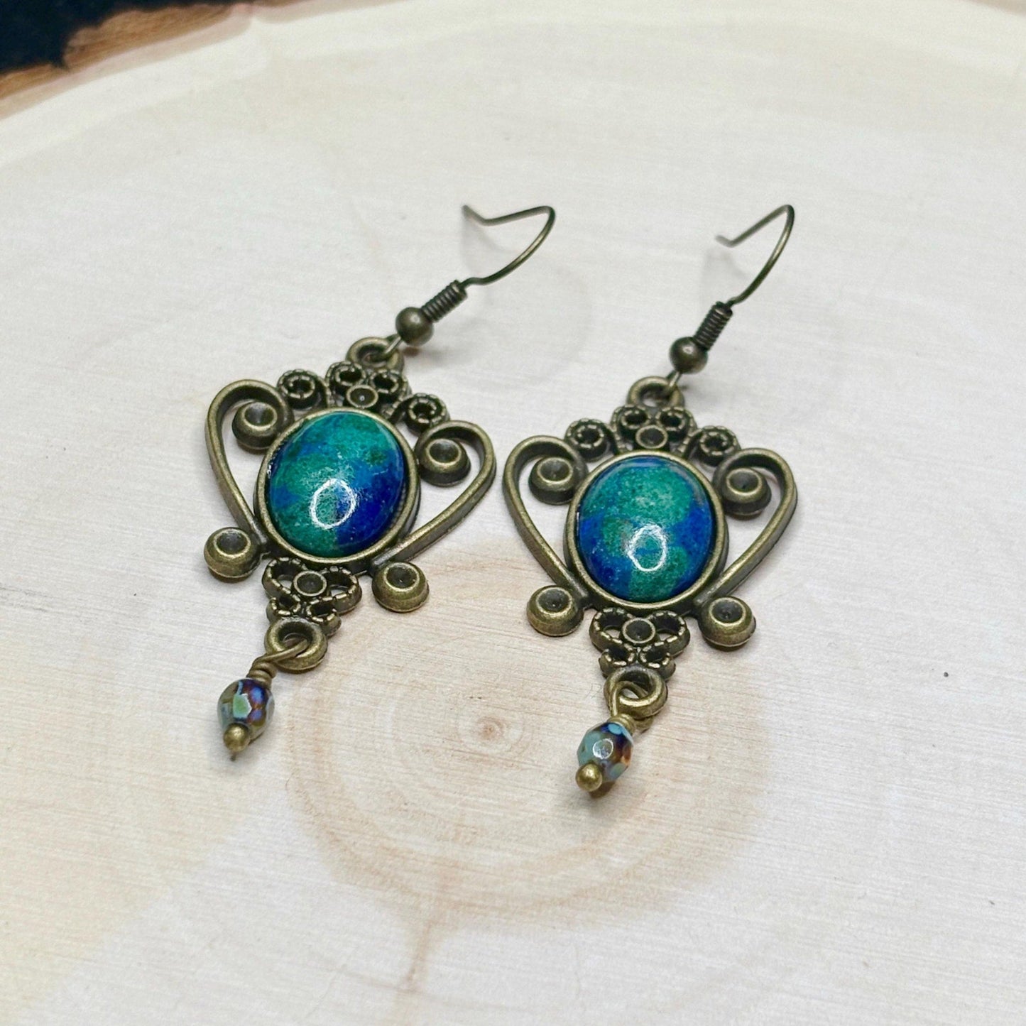 Ornate earrings with blue and green gemstones on a wooden surface
