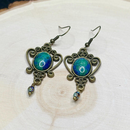 Ornate earrings with blue and green gemstones on a wooden surface