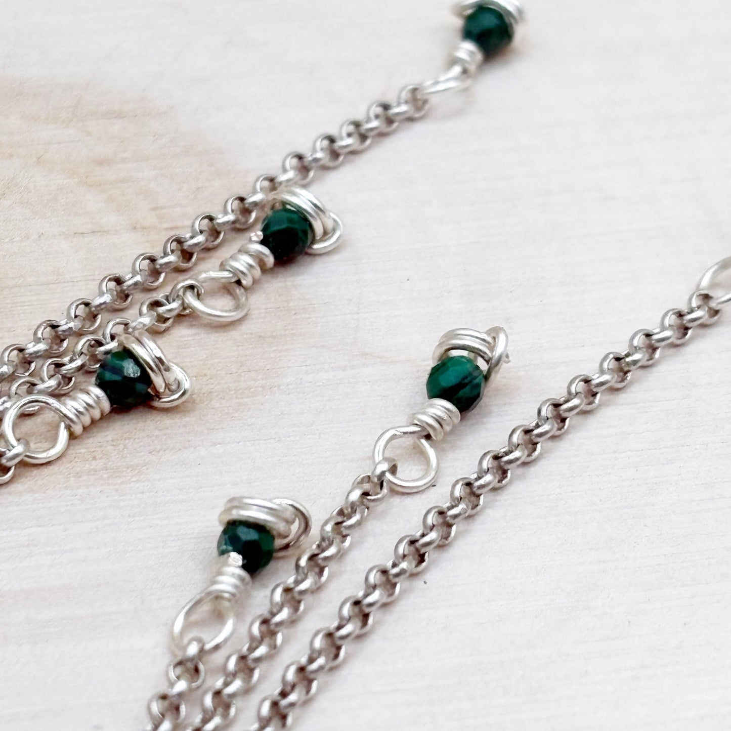 Silver chain earrings with green beads on a light wooden surface