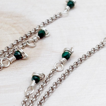 Silver chain earrings with green beads on a light wooden surface