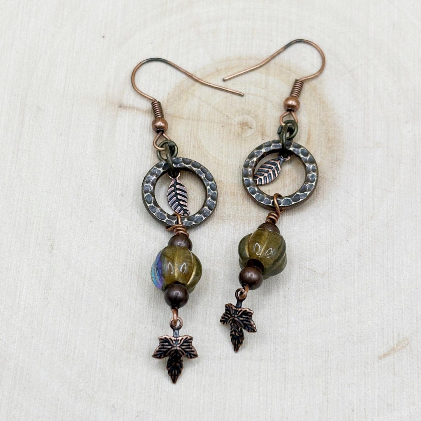 Pair of copper earrings with leaf designs and beads on a textured white background