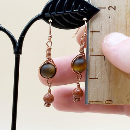 Pair of copper wire and bead earrings on a black earring stand.
