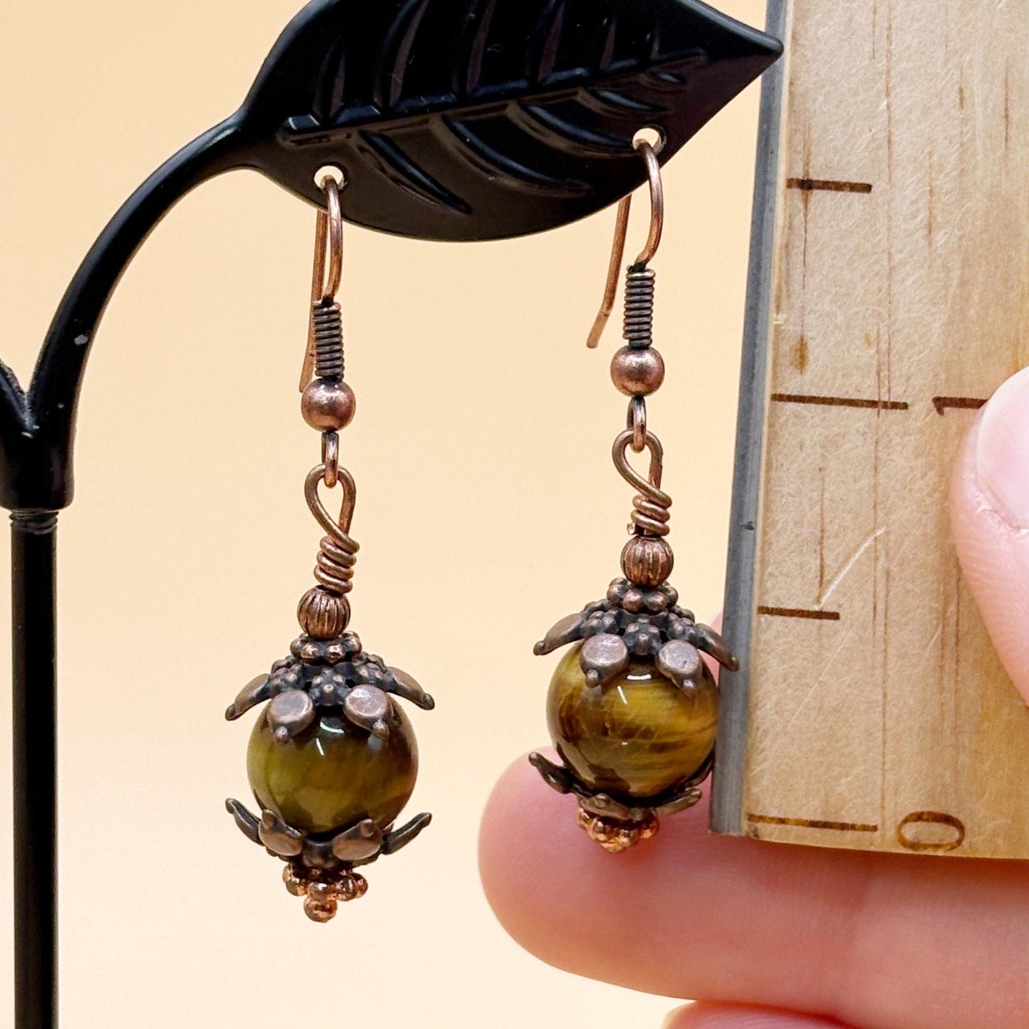 Pair of ornate earrings with brown stone beads held by a hand against a wooden background.