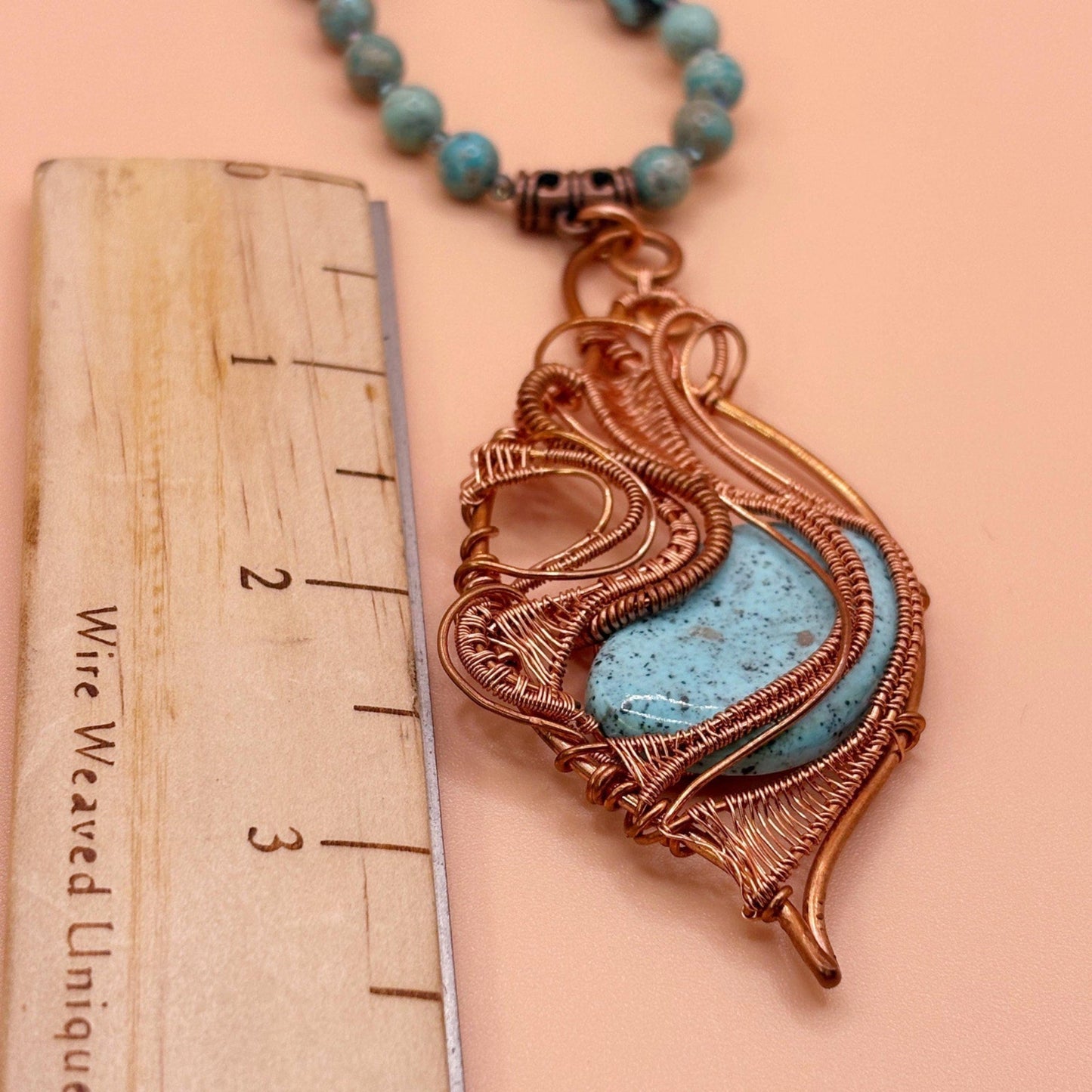 Necklace with a decorative pendant next to a ruler on a peach background