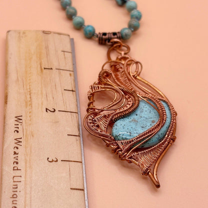 Necklace with a decorative pendant next to a ruler on a peach background