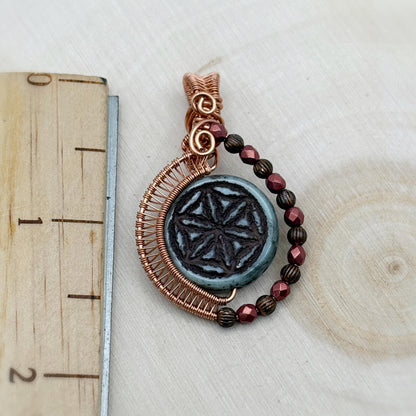Decorative pendant with beads and wirework on a wooden surface with a ruler for scale.