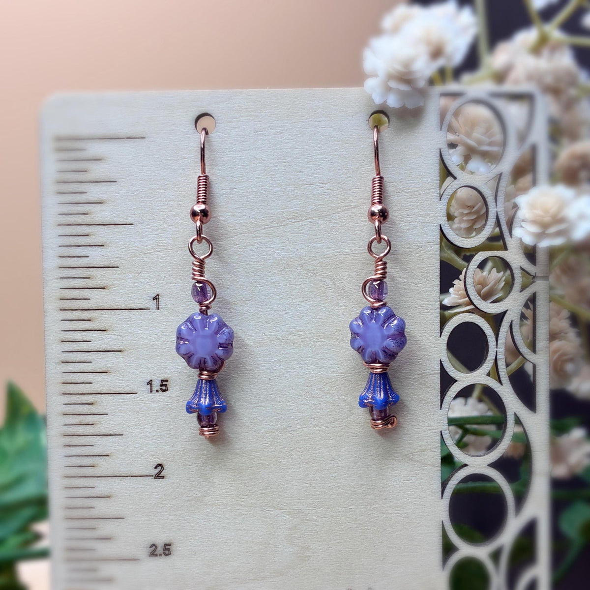 Purple floral earrings hanging on a display showing earring length