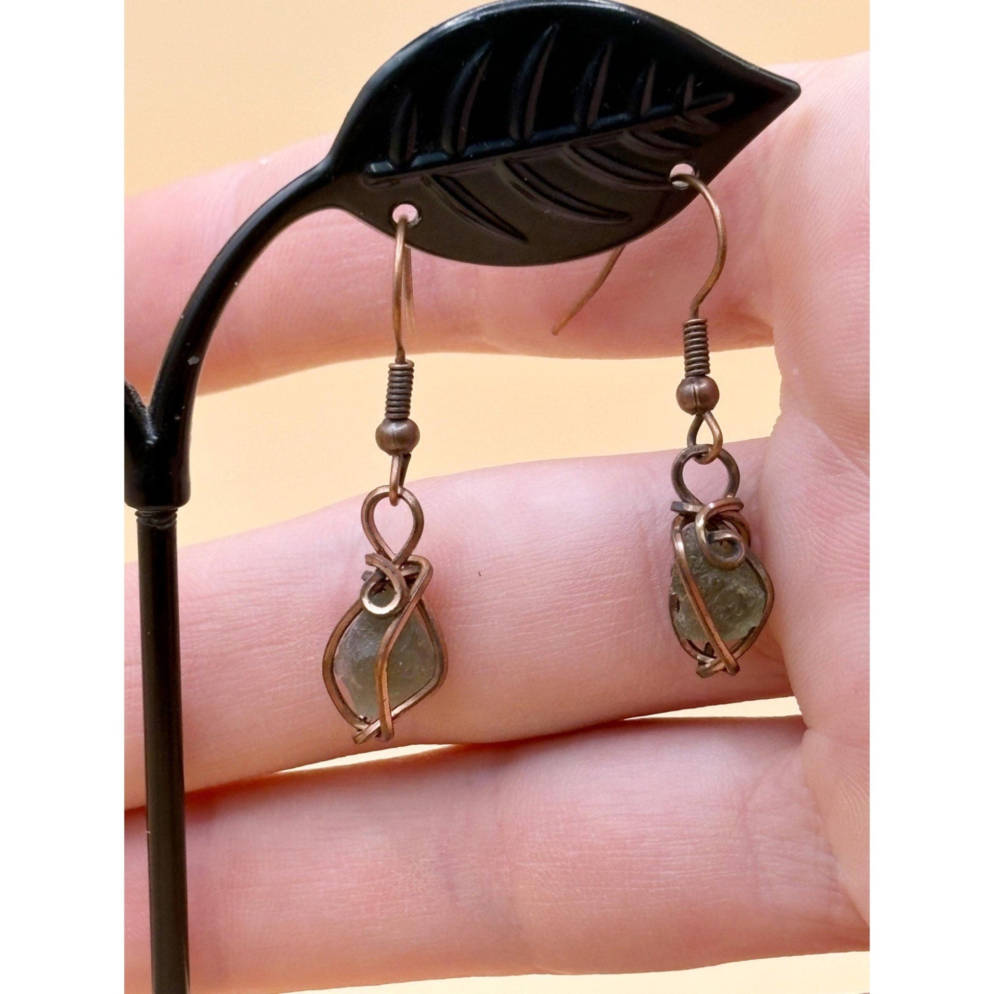 Pair of gold earrings held by a black leaf-shaped earring stand.