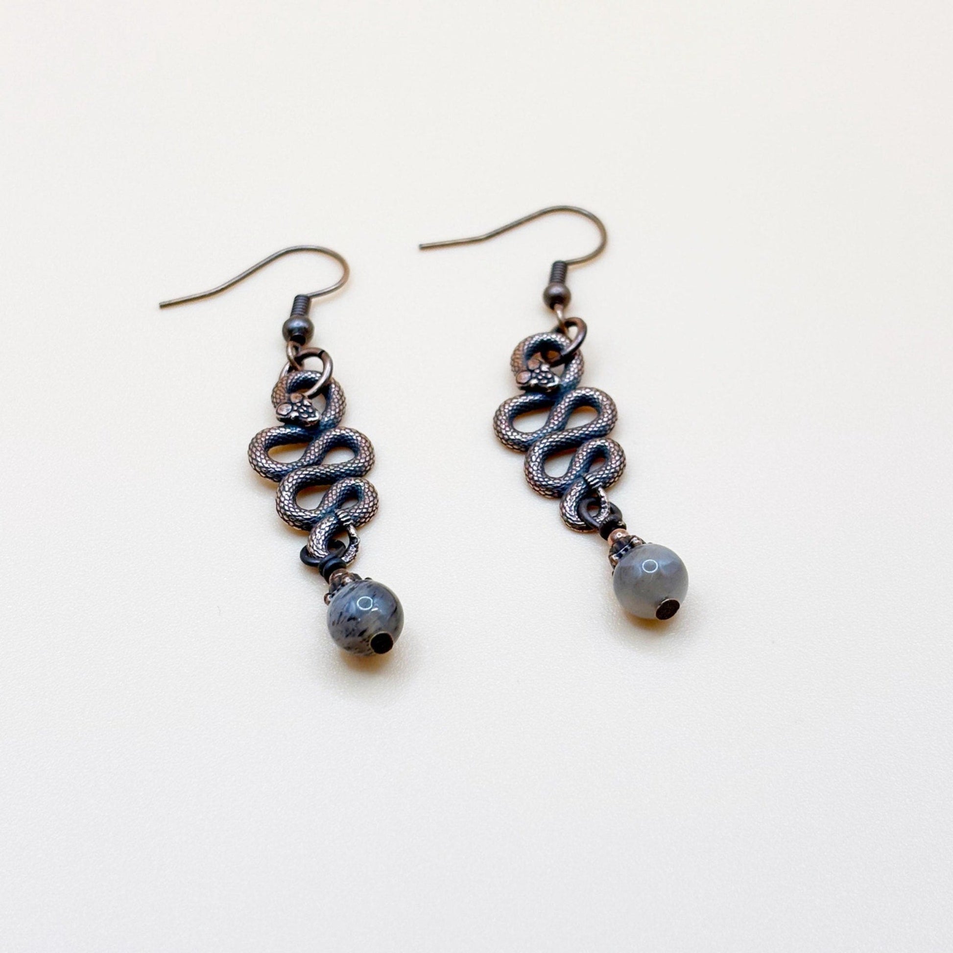 Pair of copper-colored snake-shaped earrings with a small bead on a white background