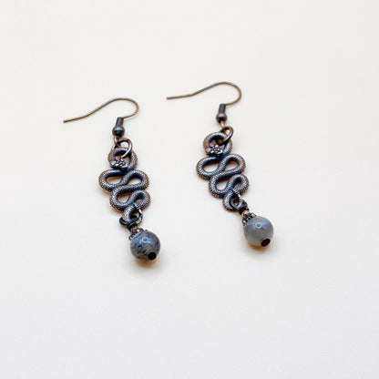 Pair of copper-colored snake-shaped earrings with a small bead on a white background