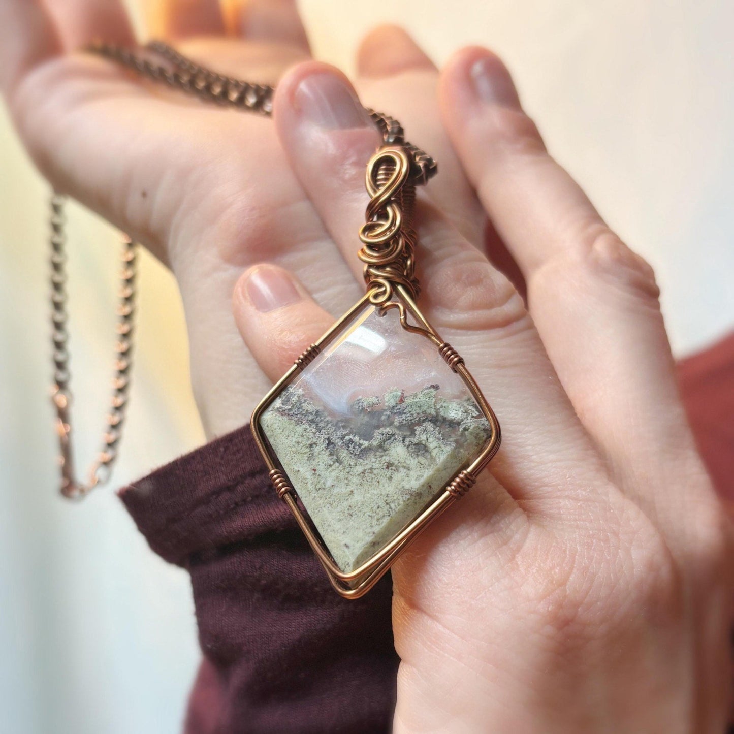 Hand holding a necklace with a square pendant featuring a scenic view.