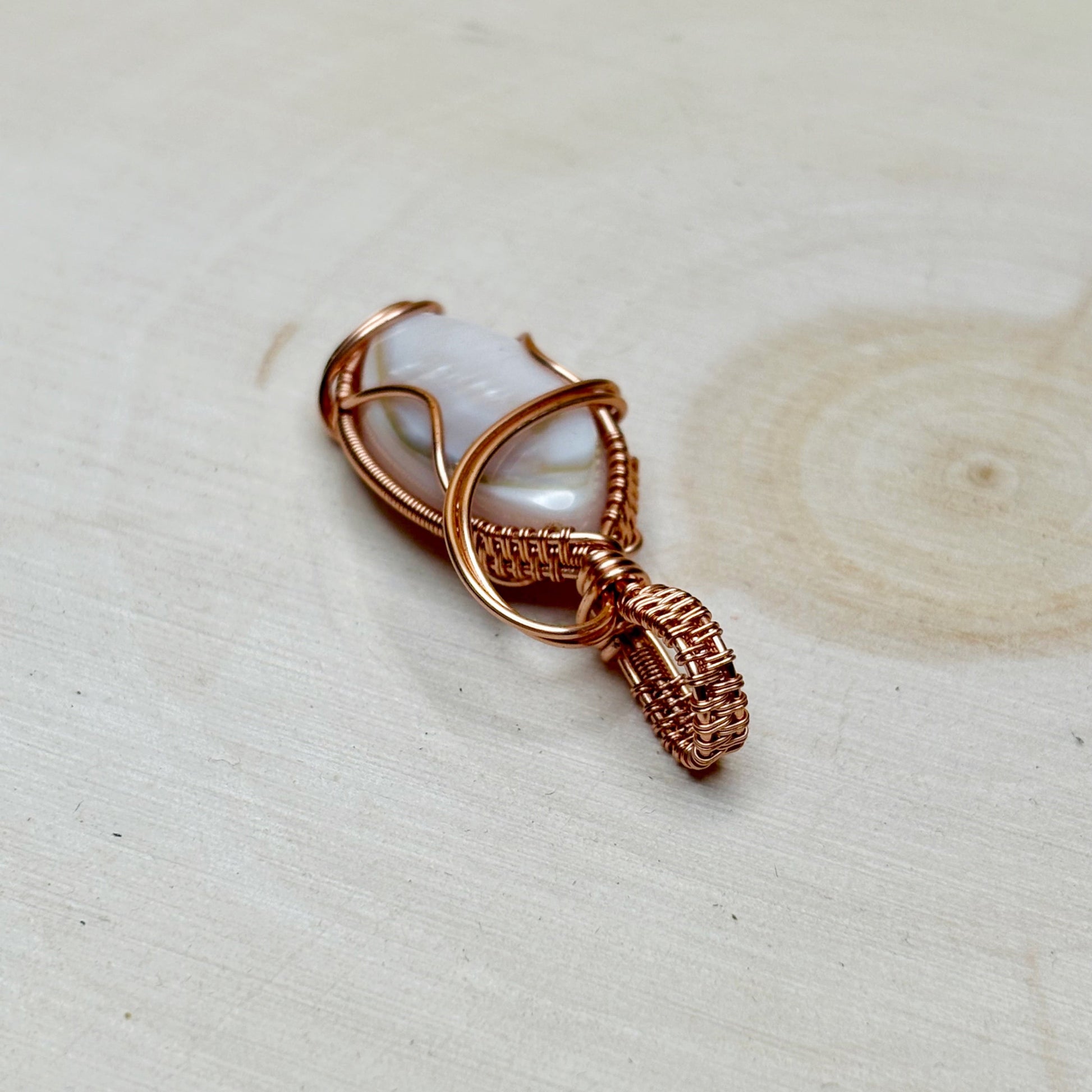 Copper wire wrapped mother of pearl shell sitting on a wooden light background